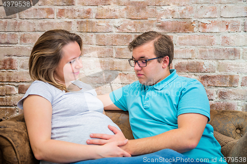 Image of Beautiful pregnant woman and man sitting near wall