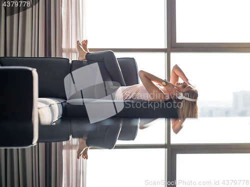 Image of Lovely Blond Woman Listening To Music while resting on couch