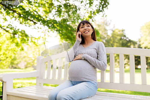 Image of pregnant asian woman calling on smartphone at park