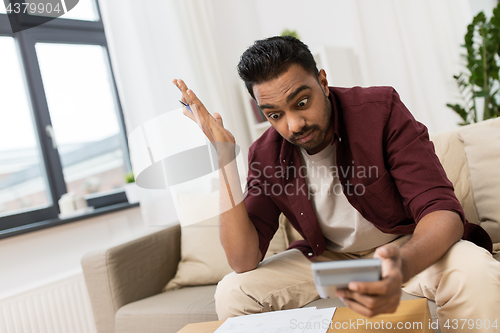 Image of confused man with papers and calculator at home