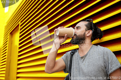 Image of man drinking coffee from paper cup over wall