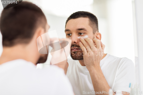 Image of young man applying cream to face at bathroom