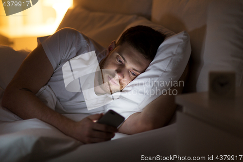 Image of happy young man with smartphone in bed at night