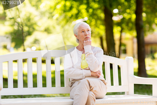 Image of sad senior woman sitting on bench at summer park