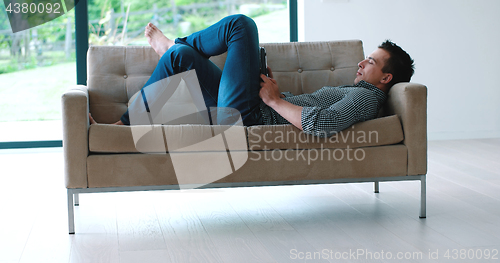 Image of Man is Laying on Couch at Home and Using Tablet