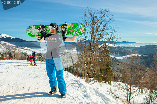 Image of Bukovel, Ukraine - December 22, 2016: Man holding his snowboard against the backdrop of mountains, hills and forests in the distance. Bukovel, Carpathian mountains