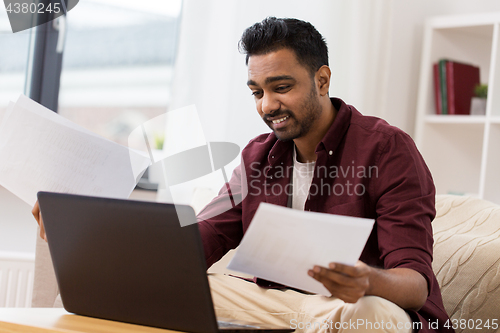 Image of confused man with laptop and papers at home