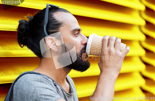 Image of man drinking coffee from paper cup over wall