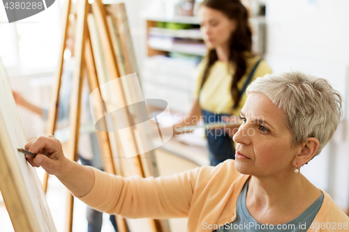 Image of senior woman drawing on easel at art school studio