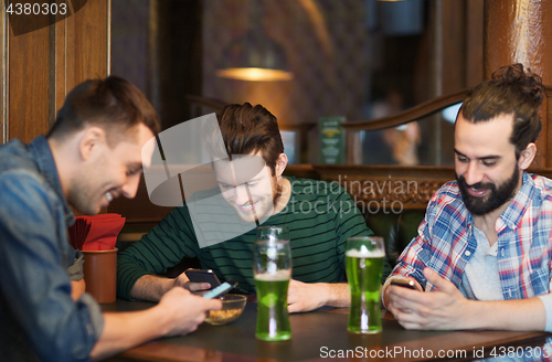 Image of friends with smartphones and green beer at pub