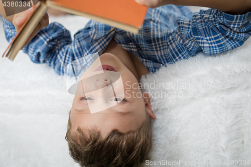 Image of little boy is lying on the bed and reading a book