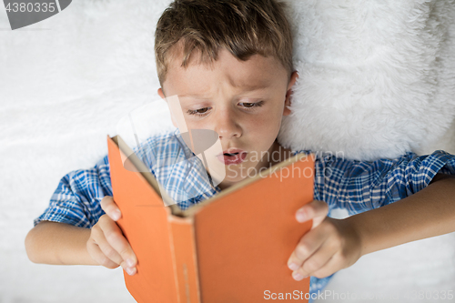 Image of little boy is lying on the bed and reading a book