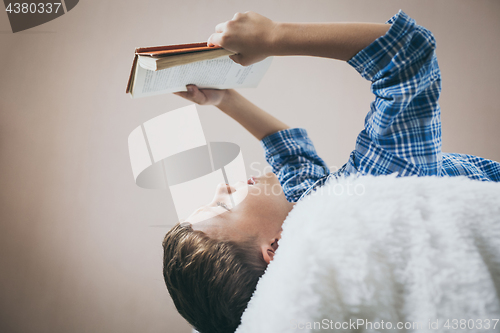 Image of little boy is lying on the bed and reading a book