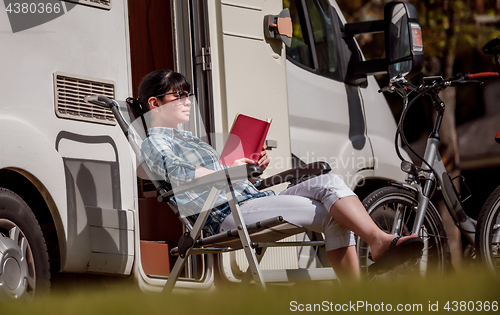 Image of Woman relaxes and reads a book near the camping .