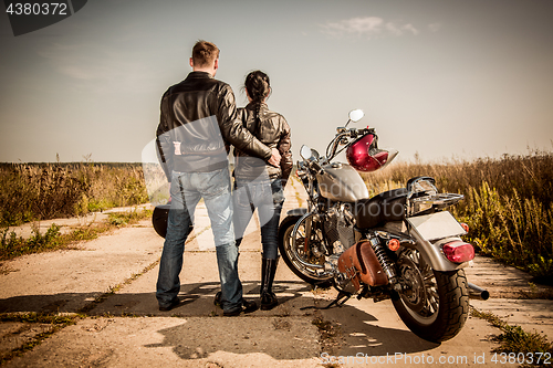 Image of Biker man and girl stands on the road and looks into the distanc