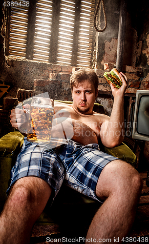 Image of Fat man eating a hamburger sitting on a chair in the slums