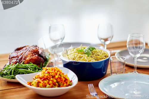 Image of pasta with basil in bowl and other food on table