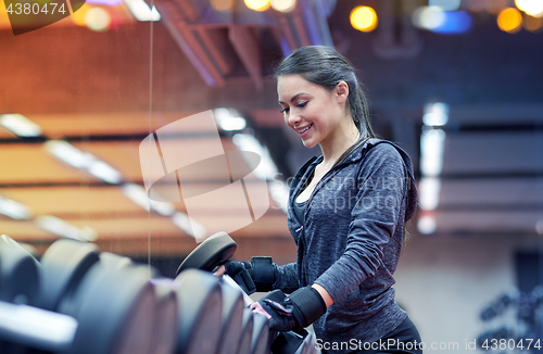 Image of young smiling woman choosing dumbbells in gym