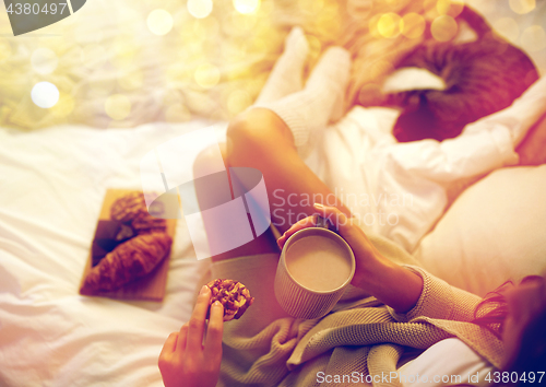 Image of close up of woman with cocoa cup and cookie in bed