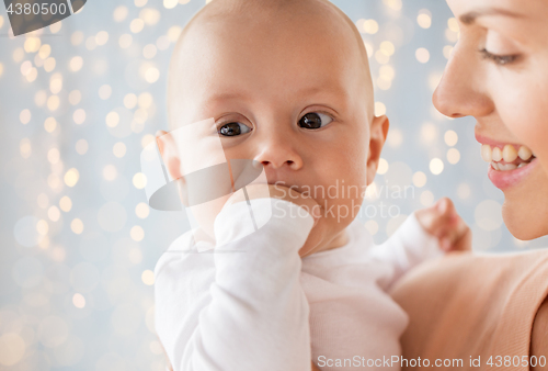 Image of happy mother with baby sucking fingers over lights