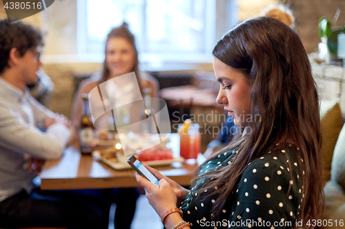 Image of woman with smartphone and friends at restaurant