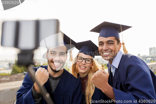 Image of happy students or graduates taking selfie outdoors