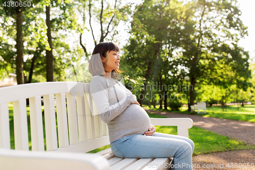 Image of happy pregnant asian woman sitting on park bench