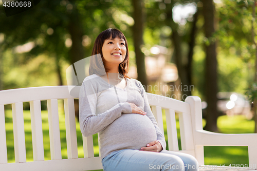 Image of happy pregnant asian woman sitting on park bench