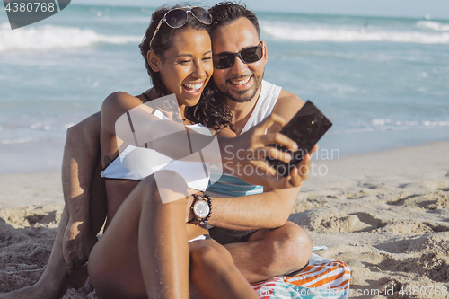 Image of Happy diverse couple taking selfie on beach