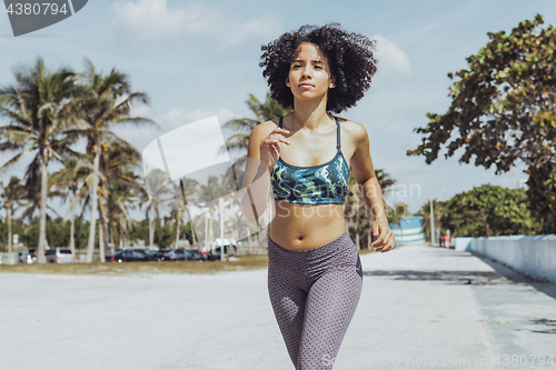 Image of Black fit girl jogging on tropical waterfront