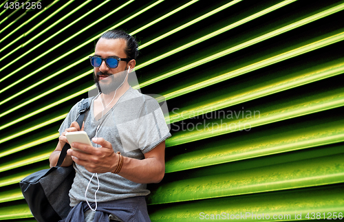 Image of man with earphones and smartphone over wall