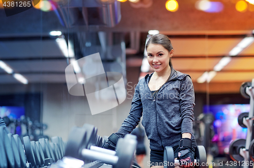 Image of smiling young woman choosing dumbbells in gym