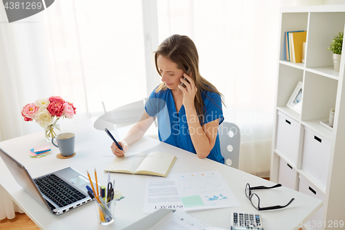 Image of woman with notepad calling on smartphone at office