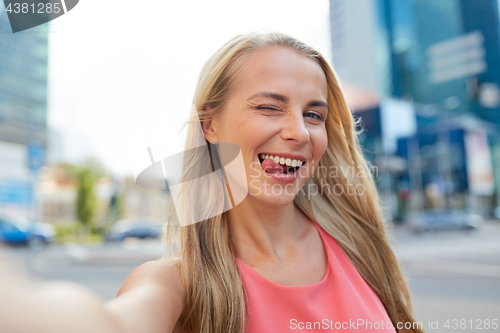 Image of happy young woman taking selfie on city street