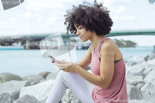 Image of Casual young woman using phone on embankment