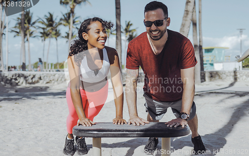 Image of Laughing sportive couple training in beach gym 