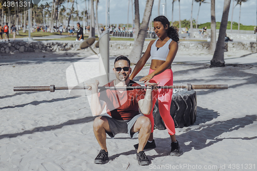 Image of Woman helping man with workout on beach
