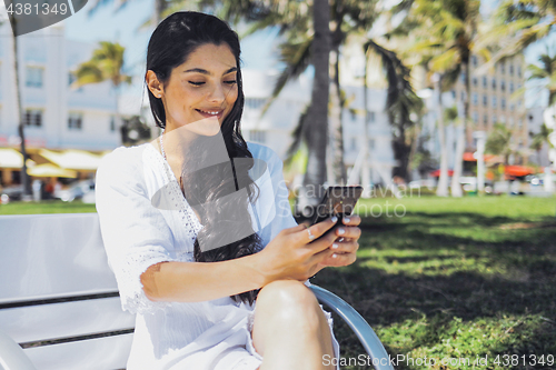 Image of Confident stylish girl using phone in park