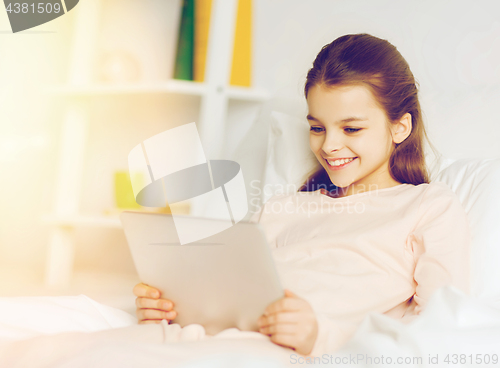 Image of happy girl with tablet pc lying in bed at home