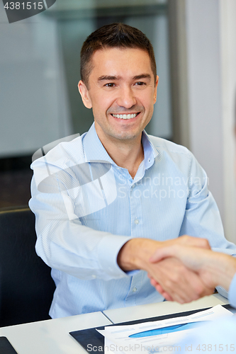 Image of smiling businessman making handshake at office