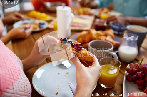 Image of hands of woman eating croissant for breakfast