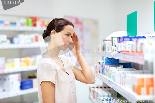 Image of customer with headache choosing drugs at pharmacy