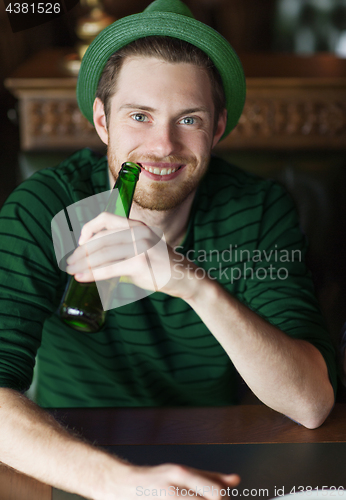 Image of man drinking beer from green bottle at bar or pub