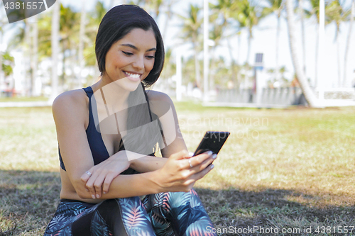 Image of Pretty sportswoman using phone in park