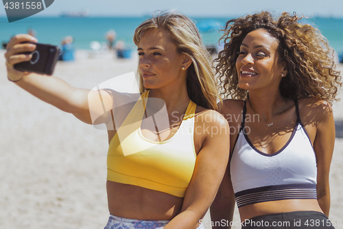 Image of Pretty diverse sportswomen taking selfie on shoreline