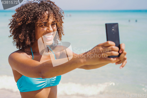 Image of Cheerful ethnic woman taking selfie on beach