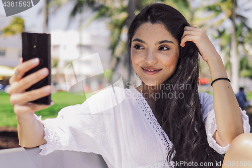 Image of Stylish girl taking selfie on bench in park