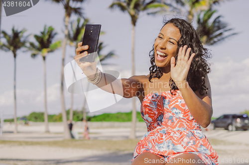 Image of Pretty black girl speaking online in park