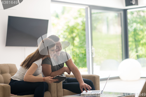 Image of couple relaxing at  home with tablet and laptop computers