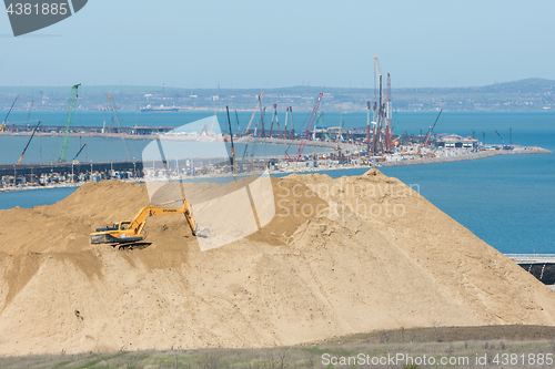 Image of Taman, Russia - 15 April 2017: A huge pile of soil in the foreground, and the bend of the bridge under construction across the Kerch Strait in the background, as of April 2017